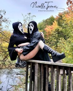 two people dressed up in costumes sitting on a wooden bridge over a body of water