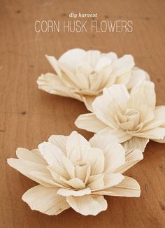 three white flowers sitting on top of a wooden table next to the words corn husk flowers