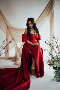 a woman in a red dress sitting on a chair next to flowers and cloths