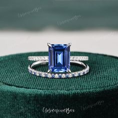 an engagement ring with a blue sapphire surrounded by diamonds on top of a green velvet box