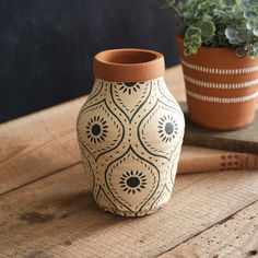 a clay vase sitting on top of a wooden table next to a potted plant