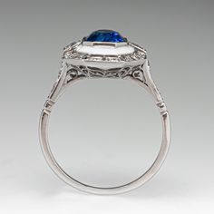 This fabulous Art Deco inspired ring is centered with one (1) cut-cornered rectangular cut natural sapphire that is bordered with white enamel. The ring is accented with two (2) square French cut diamonds, and twenty-two (22) bead set round brilliant and old European cut diamonds. The ring is bordered with milgrain edging. It measures 16.2mm at the top, rises 6.8mm above the finger, tapering to 1.9mm wide and 1.1mm thick at the base of the shank. It is currently a size 7. Luxury Square Cut Sapphire Ring, White Gold Enamel Rings With Polished Finish, White Diamond Gemstone Ring In Art Deco Style, Luxury White Gold Enamel Oval Ring, White Sapphire Platinum Ring In Fine Jewelry Style, Art Deco Sapphire Ring With Halo Setting, Polished Enamel Rings In Fine Jewelry Style, Luxury Formal Enamel Ring With Gemstone, White Sapphire Ring In Platinum