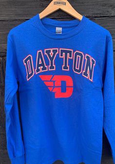 Show off your team pride in this Dayton Flyers Blue Arch Logo Long Sleeve T Shirt! This Dayton Long Sleeve Tee features a screen print of "Dayton" with Flyers logo across chest. Make sure everyone knows you root for the Flyers with this Blue Dayton T Shirt. Go Flyers!! Classic fit, Seamless double needle 7/8" collar, Taped neck & shoulders, Ribbed cuffs, Unisex, Fit: True to Size, 100% Cotton Long Sleeve Cotton T-shirt With University Logo, University Logo Long Sleeve Cotton T-shirt, Blue Long Sleeve T-shirt For School Spirit, Blue Long Sleeve Fan Merchandise T-shirt, Blue Long Sleeve T-shirt With Team Spirit, Blue Long Sleeve T-shirt For College, Blue Long Sleeve T-shirt For Sports Events, Dayton Flyers, Arch Logo