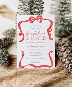 a red and white bridal shower card with pine cones on the table next to it