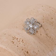 a diamond flower ring sitting on top of a piece of rock with sand in the background