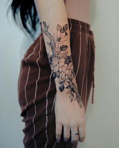 a woman's arm with flowers on it and a bird perched on the branch