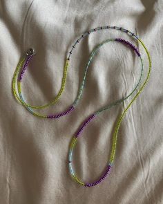 a beaded necklace is laying on a white sheet with purple and green beads hanging from it's end