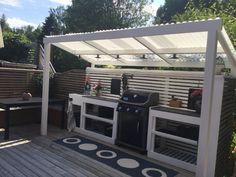 an outdoor bbq with grills and seating on the back deck, surrounded by greenery