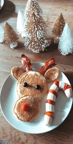 a white plate topped with pancakes covered in bacon and a reindeer face made out of fruit