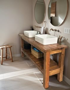 two sinks are sitting on a wooden table in the middle of a room with mirrors and stools