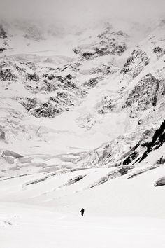 two people are skiing down a snowy mountain side with mountains in the background and one person is on skis