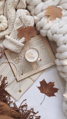 an open book, coffee cup and autumn leaves on a white blanket with woolen