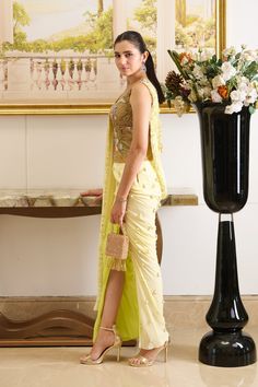 Rhyming perfectly with your day-time soirees, Lulu is a pre-stitched saree featuring a golden-hued designer blouse made out of fish-net fabric with floral embroidery detailing and a front pallu. The innovative draping style creates an exquisite piece immersed in the complimentary palette of lemon, presenting a fresh look for seasonal affairs. A perfect amalgamation of modernity and sophistication indulged in the traditional silhouette is a must-have festive essential that your wardrobe has been missing out on. Sleeveless blouse crafted out of fish-net fabric and adorned with beautiful floral embroidery detailing. The pre-draped skirt featuring a slit is adorned with dainty detailing of embroidered drops. Front pallu embellished with a linear sequined pattern and floral cut-work detailing a Stitched Saree, Fish Net, Embroidery Detailing, Draped Skirt, Net Fabric, Designer Blouse, Cut Work, Pale Green, Embroidery Details