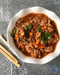 a white bowl filled with meat and vegetables next to chopsticks