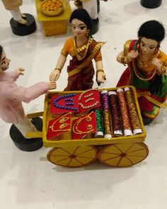 two figurines are on display in front of an elaborately decorated tray with beads