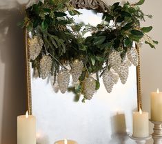 some candles are sitting on a mantle with greenery and lace hanging from it's sides