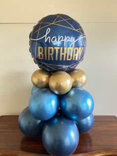 blue and gold balloons are stacked on top of each other in front of a happy birthday sign