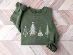 a green sweater with trees on it sitting on a wooden floor next to a pair of scissors