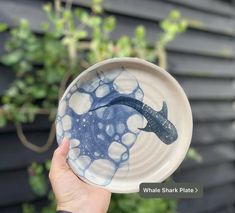 a hand holding a blue and white plate with a fish on it