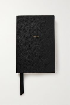 a black notebook with gold lettering on the front and side, sitting on top of a white surface