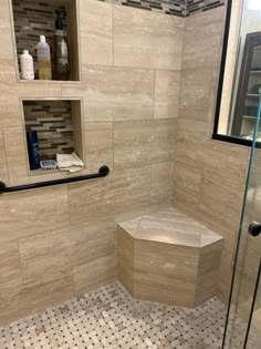 a walk in shower sitting next to a glass door and tiled floored area with shelves on the wall