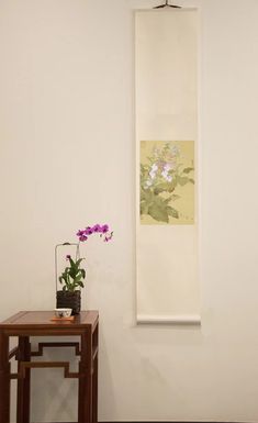 a vase with flowers sitting on top of a wooden table next to a white wall