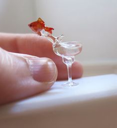 a tiny wine glass sitting on top of a white table next to a person's hand