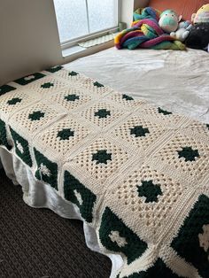 a crocheted blanket on top of a bed next to a window with stuffed animals