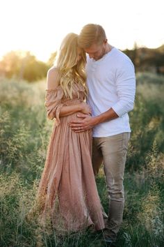 a pregnant couple standing in tall grass at sunset