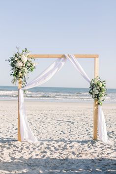 a wedding arch on the beach with white flowers and greenery for an outdoor ceremony