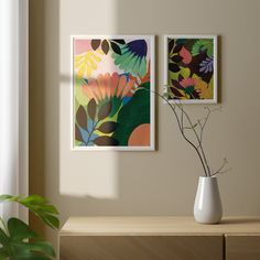 two paintings hang on the wall next to a vase with flowers in it and a plant