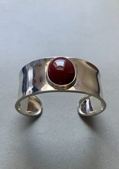 This beautiful cuff bracelet features a central carnelian stone with no imperfections. The metal is sterling silver, and the bracelet is 6", although the gap between the ends of the cuff make it fit perfectly for medium-sized wrists. It is a Taxco bracelet that was made in Mexico. Vintage Silver Cuff Bracelet, Adjustable Vintage Sterling Silver Cuff Bracelet, Handmade Red Sterling Silver Cuff Bracelet, Adjustable Silver Vintage Cuff Bracelet, Elegant Red Sterling Silver Cuff Bracelet, Gem Bracelets, Silver Jewelry Bracelet, Quoi Porter, Carnelian Stone