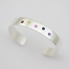 "This lovely cuff bracelet has a variety of birthstones to represent your family. You can choose to have up to 15 stones and they can be arranged in a staggered position (shown) or in a straight line. Please make your selection when adding this item to your cart.  The cuff is 10mm wide and 2mm thick and has 3mm round, faceted gemstones of your choice. Please specify which stones and the order you need them in along with your wrist size at the checkout in \"note to seller\".  The bracelet has a beautiful hand hammered finish, and the birthstones are flush set. Comes with a polishing cloth, care card, gift box, and a lifetime warranty. This item is made to order, please allow up to 3 weeks for fabrication." Birthstone Jewelry Mothers, Pearl Drop Pendant, Straight Line, Silver Prices, Card Gift, Care Card, Pearl Charms, Faceted Gemstones, Drop Pendant