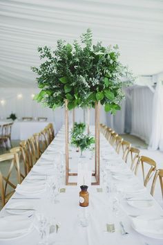 there is a long table set up with white linens and greenery in vases