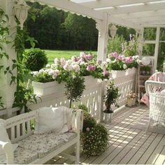 a white bench sitting on top of a wooden deck next to flowers and potted plants