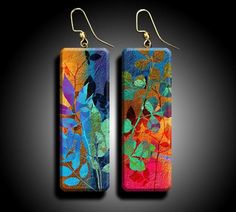 pair of earrings with colorful leaves on them, hanging from hooks against a black background