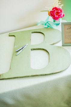 there is a small wooden letter on top of a table next to a vase with flowers