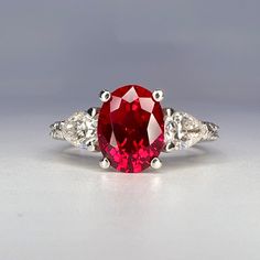 a red and white diamond ring with three diamonds on the side, set in 18k white gold