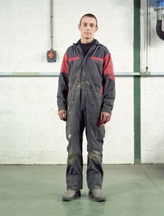 a man standing in front of a white wall wearing a black and red coverall