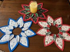 three paper flowers sitting on top of a wooden table next to a candle and some candlesticks