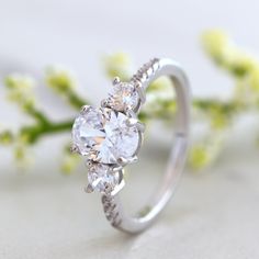 an engagement ring with three stones on the side and flowers in the back, sitting next to it