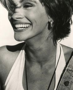 a black and white photo of a woman with short hair smiling at the camera while wearing necklaces