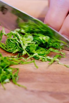 a person is cutting up some greens on a wooden table