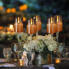 candles are lit on the centerpieces of a table set with flowers and wine glasses