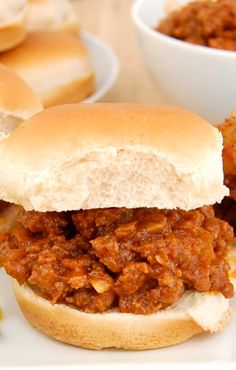 a sloppy joe sandwich on a plate with pickles and other food items in the background