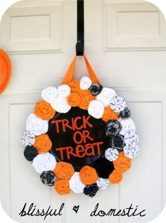 a trick or treat wreath hanging on a door with an orange and white ribbon around it