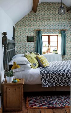 a bed sitting under a window in a bedroom next to a wooden table and chair