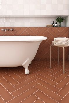 a white bath tub sitting on top of a bathroom floor next to a wooden stool