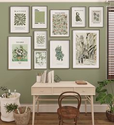 there are many framed pictures on the wall next to a desk with a chair and potted plant