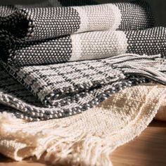 several blankets stacked on top of each other next to a wooden table with a black and white striped blanket